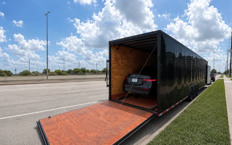 A black enclosed trailer with its ramp down and a Mercedes sedan secured inside.